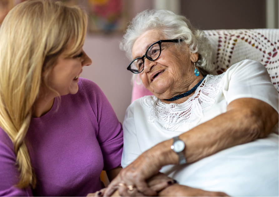 Two women are talking, one is seated and the other is leaning over.