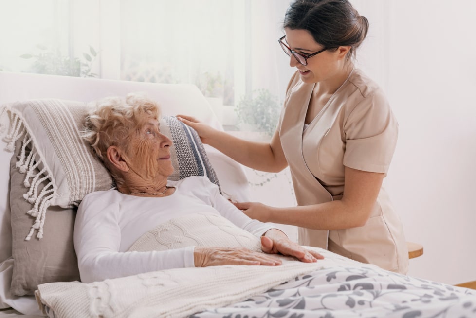 A nurse at the bedside of an elderly woman in hospice care