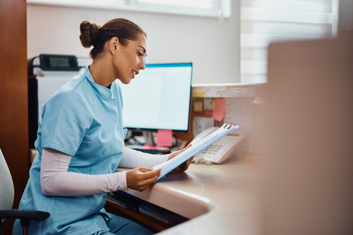 Young nurse going through medical records at reception desk in hospital.