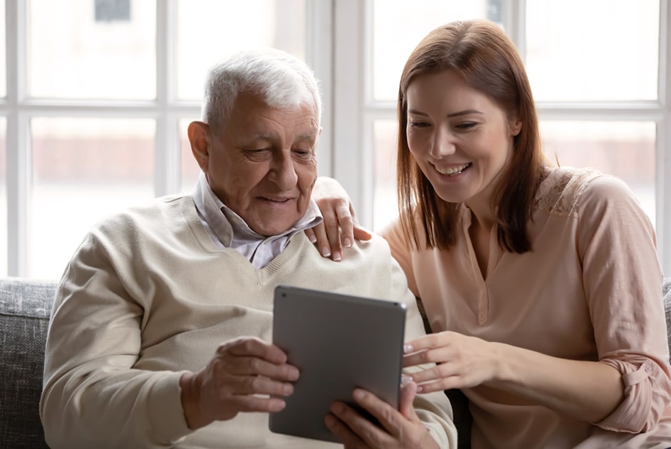 An elderly man is showing a tablet device to a younger woman