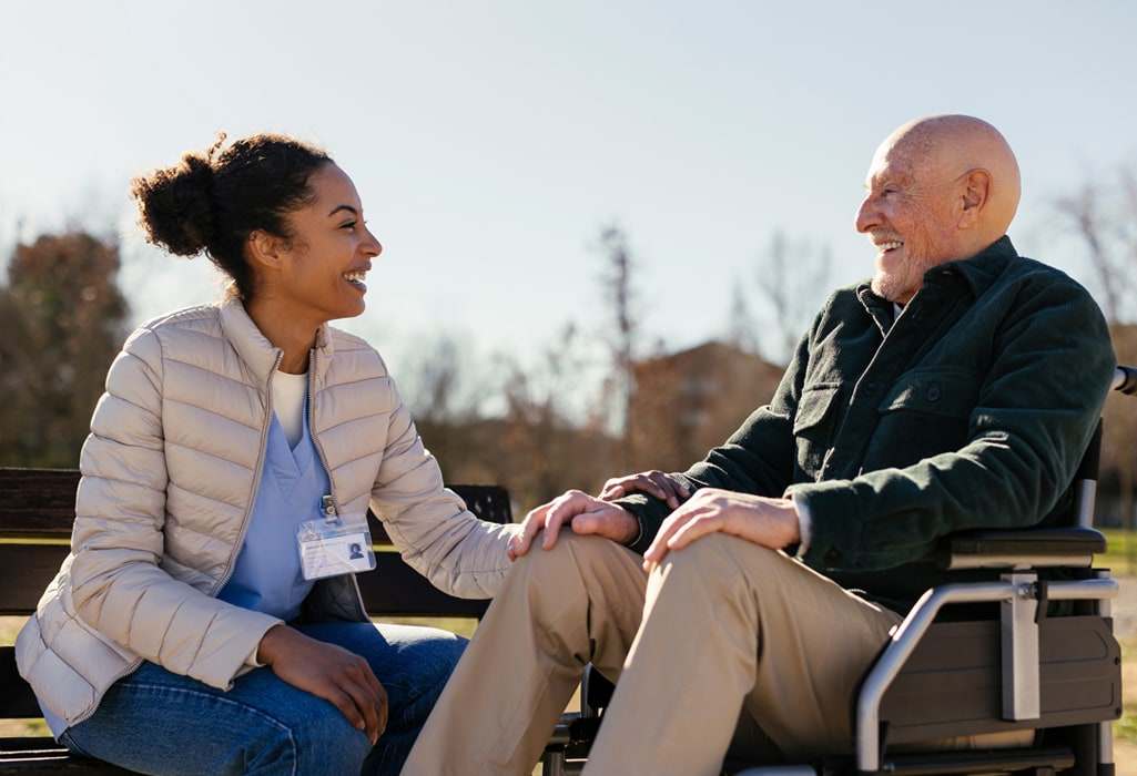 Happy caretaker with senior man sitting on wheelchair in park