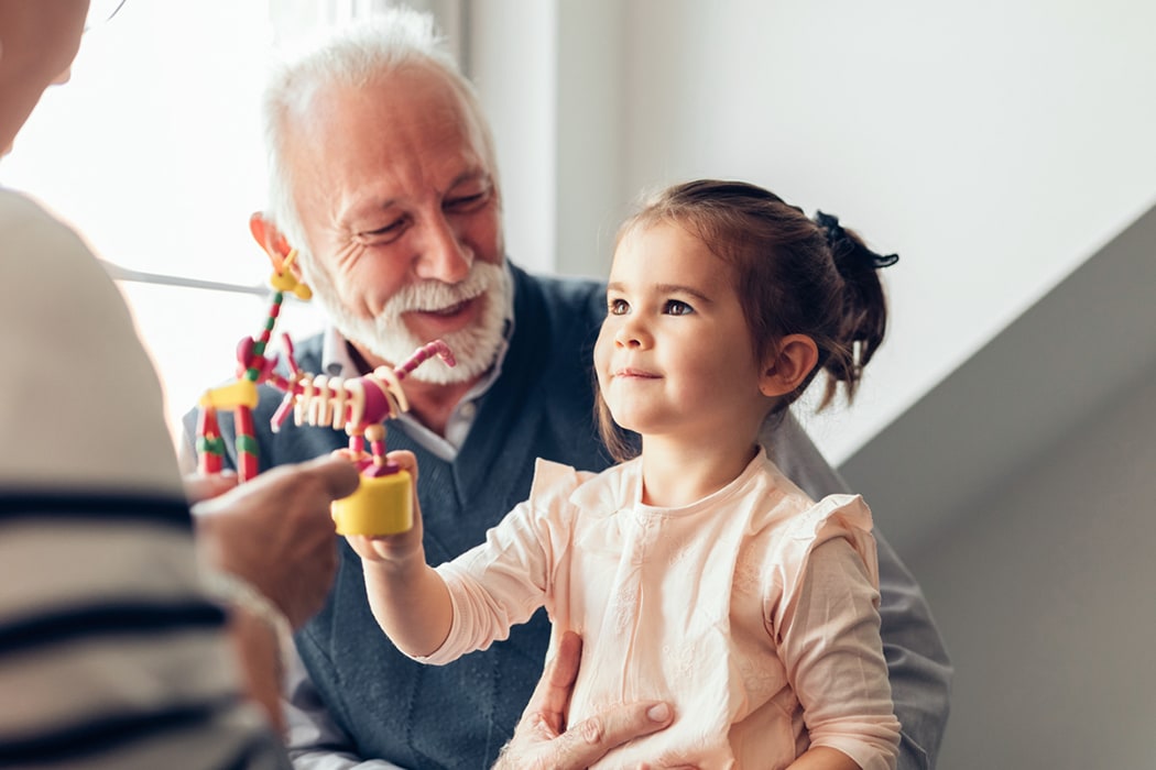 A elderly man is playing with a young female child