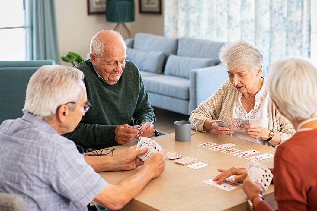 A group of four elderly people are seated around a table playing a card game