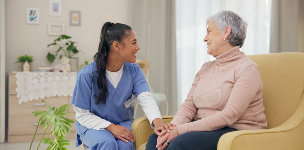 A healthcare worker is embracing a seated older woman