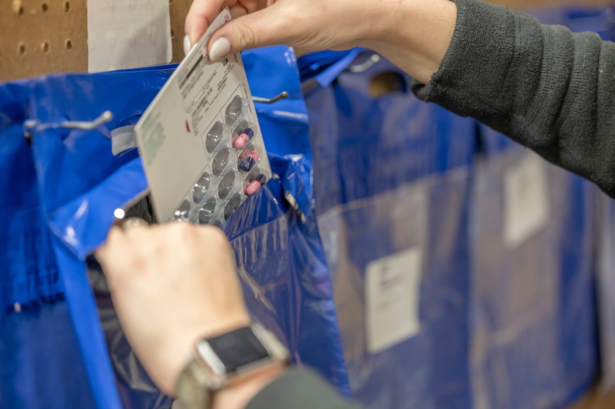 A person is placing medication in a blue plastic bag