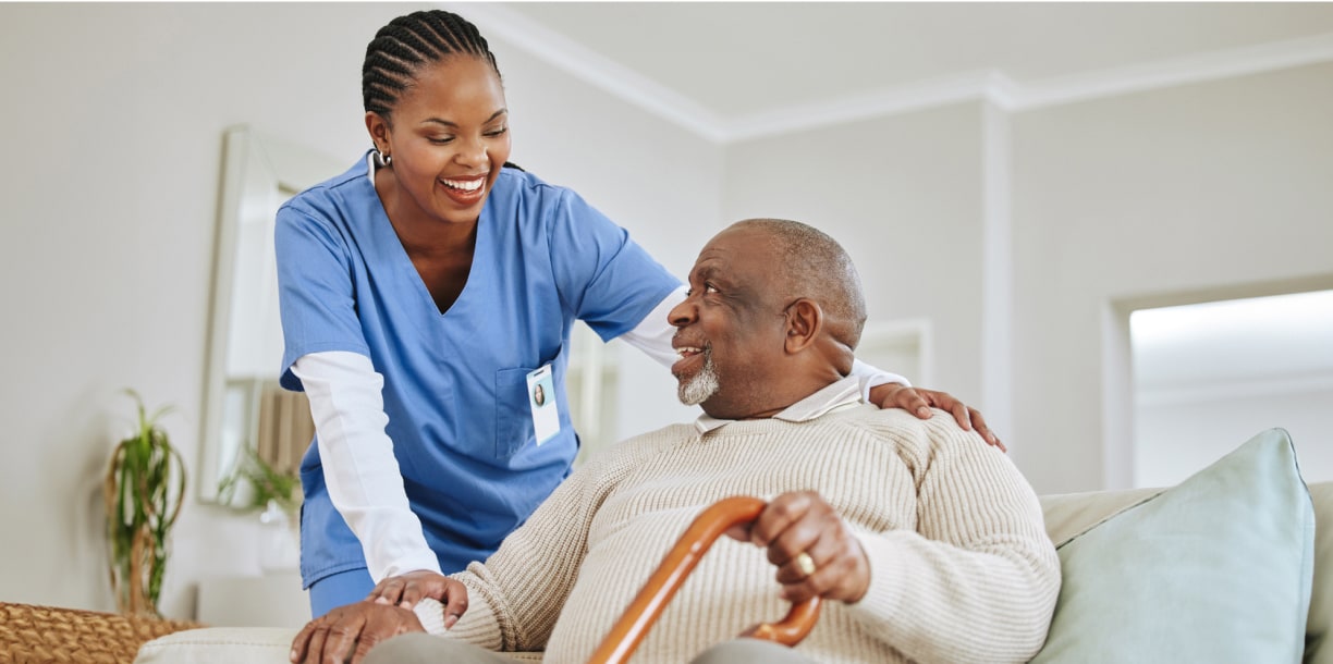 Health care staff working, leaning over to help an elderly man with a cane