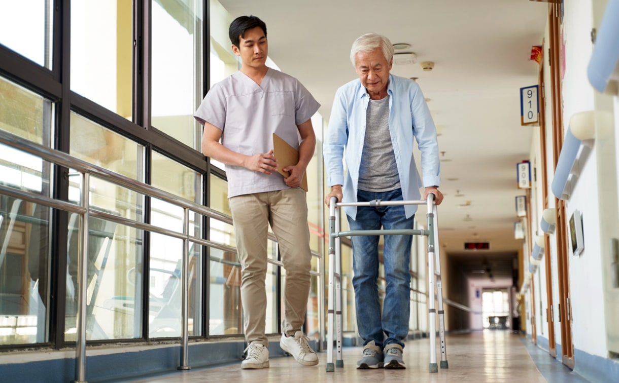 Health care worker assisting an older man using a walker in a rehab center