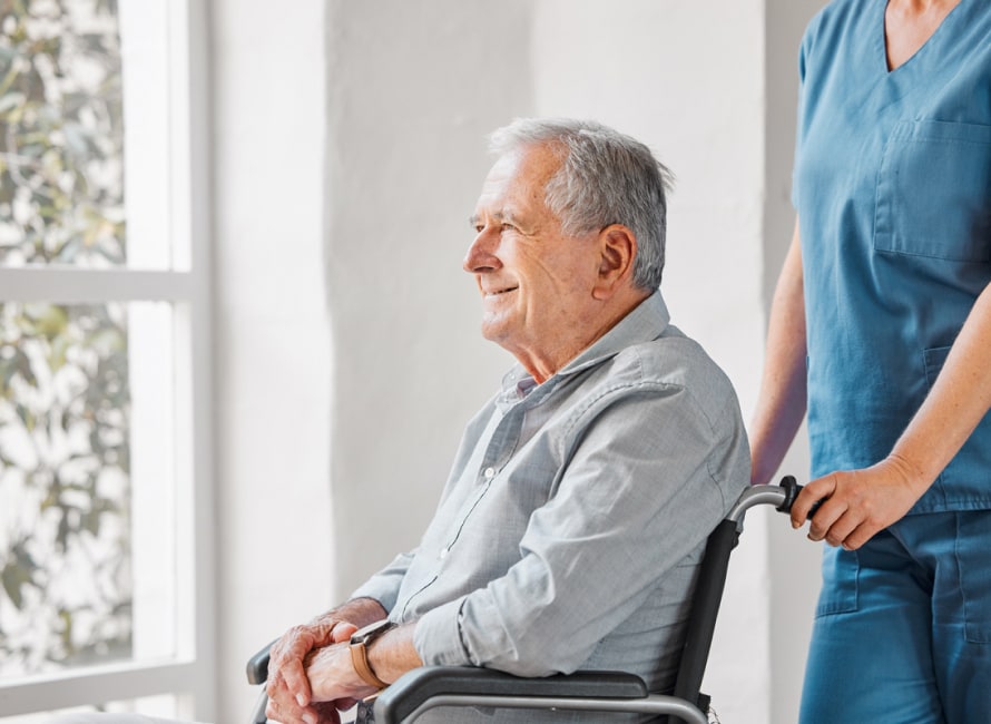 An elderly man in a wheelchair is looking out a window